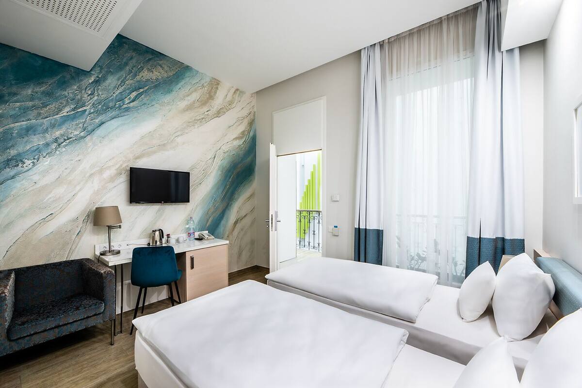Hotellihuone, jossa on marmoriseinä, työpöytä tuolilla, kaksi sänkyä ja televisio.