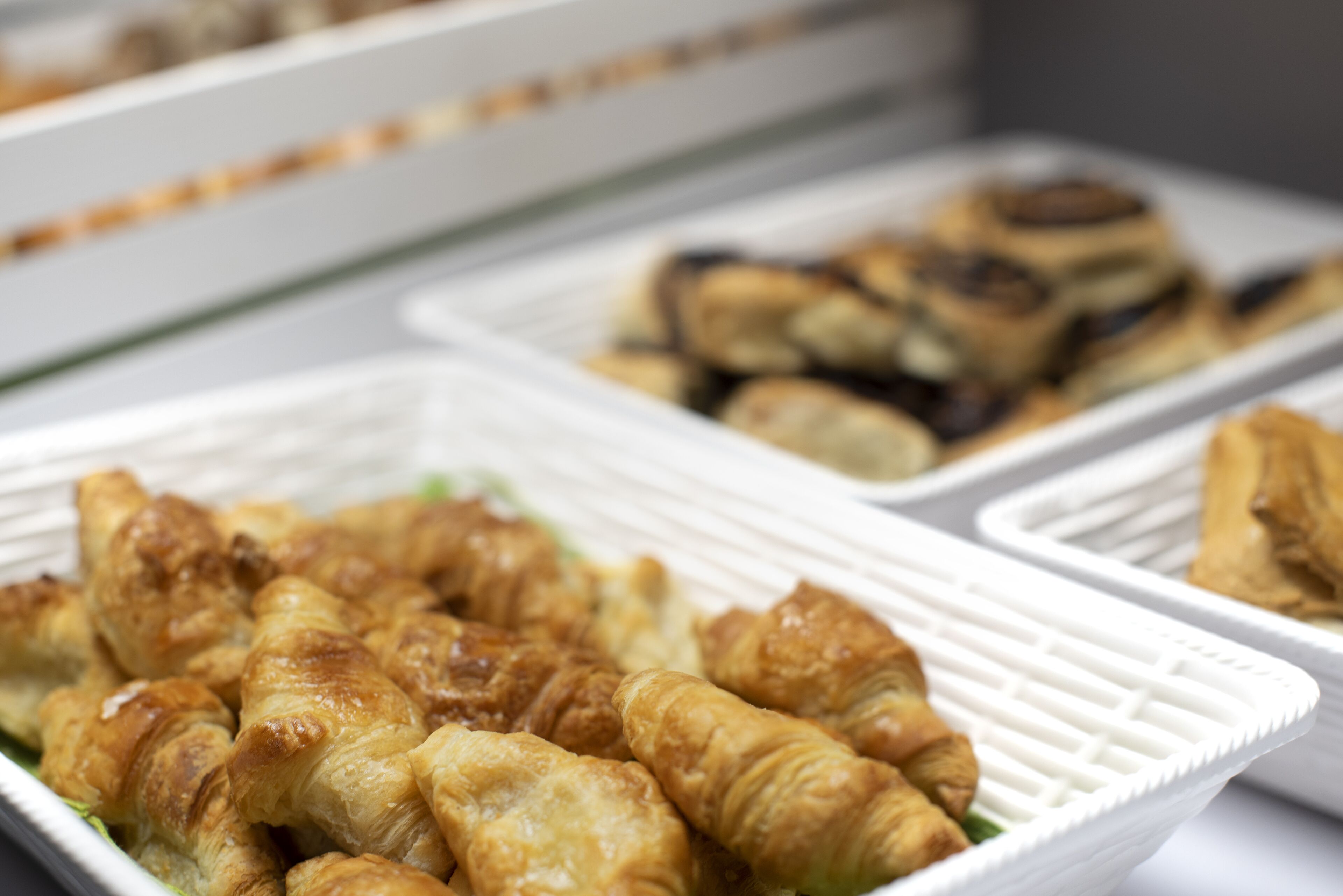 Un bufé con bandejas de pastelería, incluyendo cruasanes y otros productos horneados.