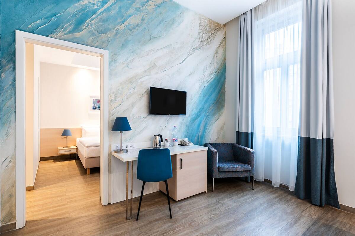 Hotellihuone, jossa on marmoriseinä, työpöytä tuolilla, työpöydän yläpuolelle asennettu televisio ja ikkuna, jossa on verhot.