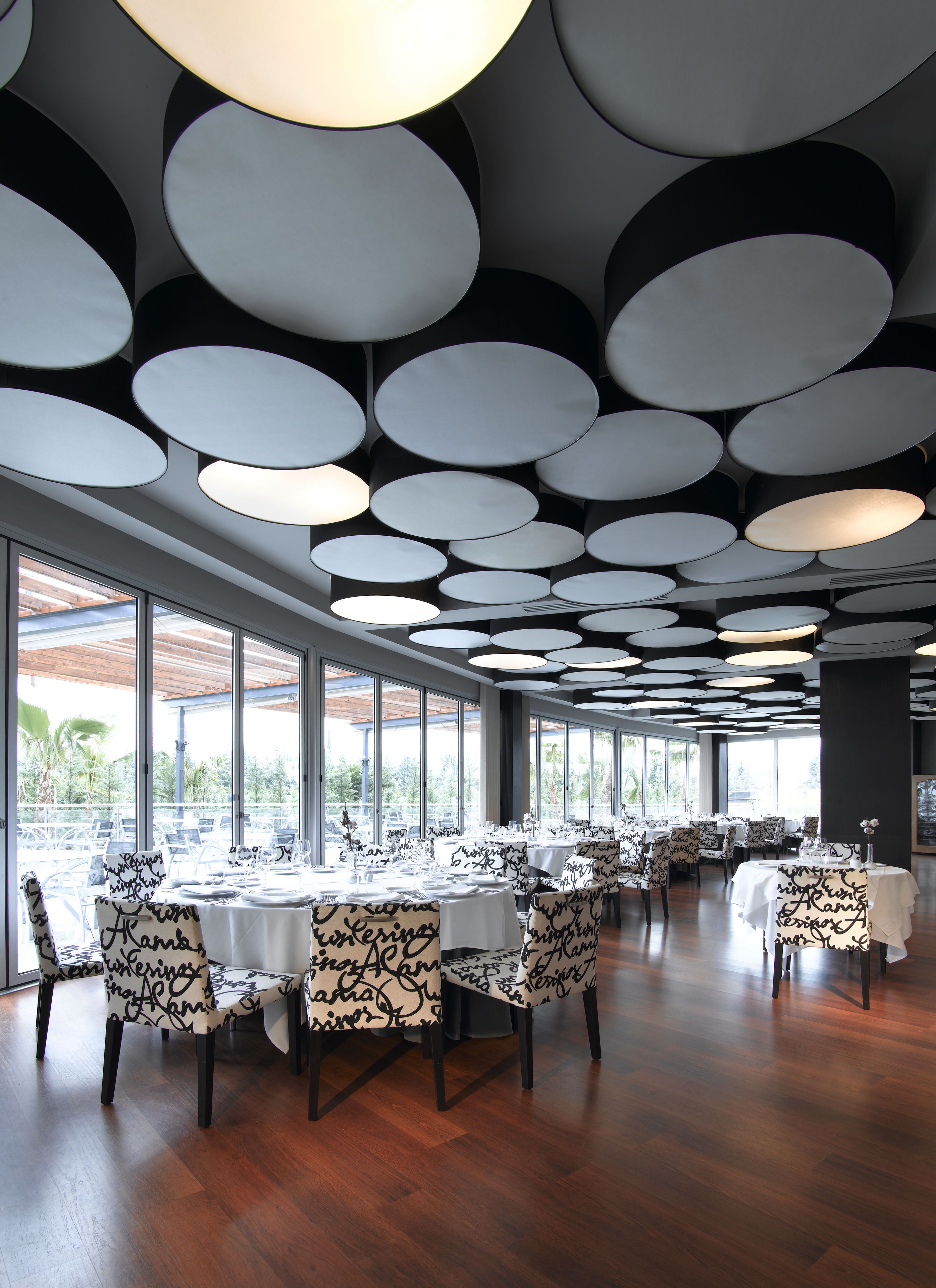 A dining area with round tables, chairs, and a ceiling with circular light fixtures.