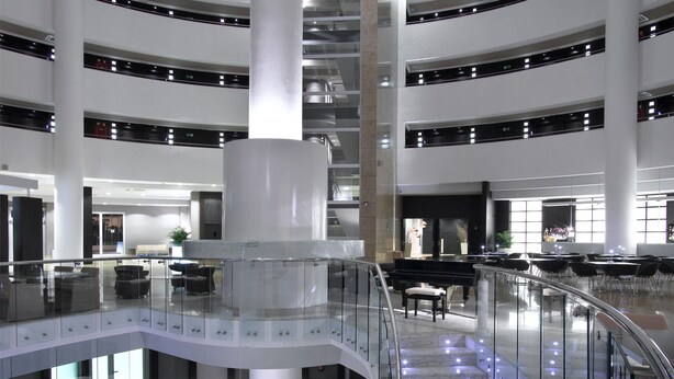 Un interior moderno con una escalera curva, barandillas de cristal y una columna central.