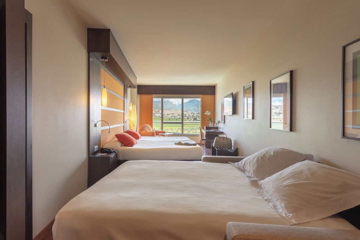 Une chambre d’hôtel avec deux lits, un bureau, une chaise et une grande fenêtre donnant sur les montagnes.