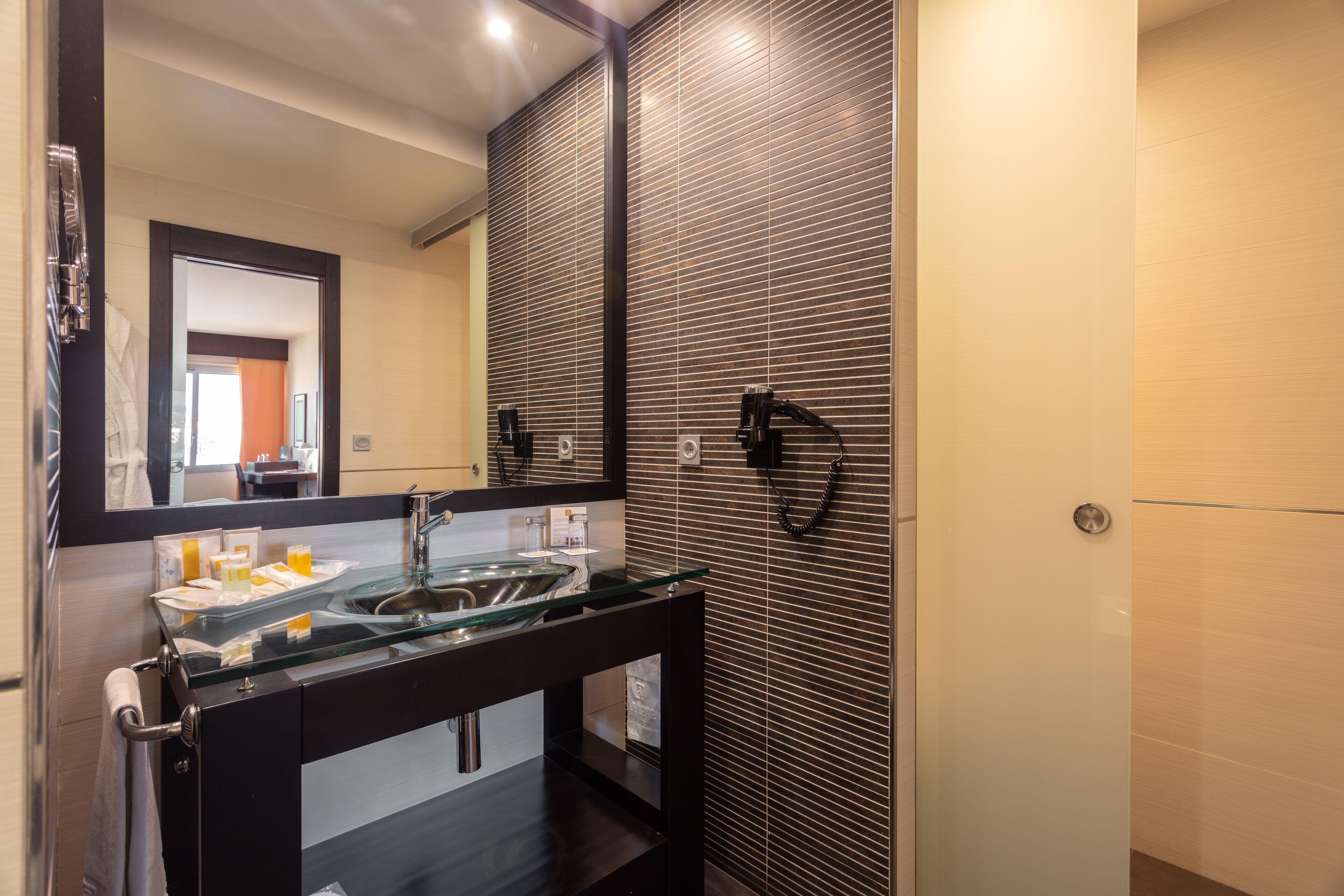 Un baño moderno con un lavabo de vidrio, muebles oscuros y un espejo grande.