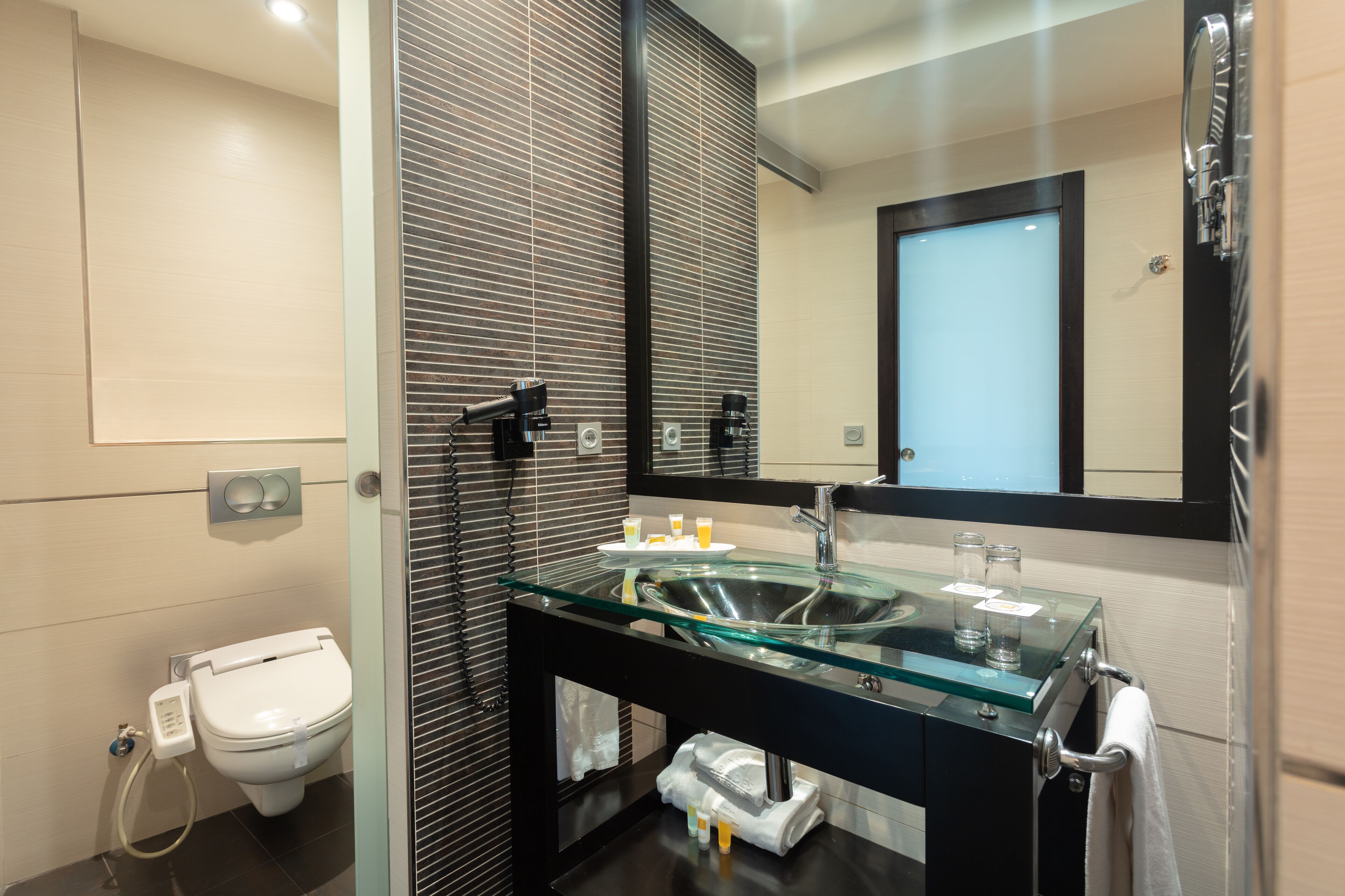 Un baño moderno con un lavabo de vidrio, un inodoro y un espejo grande.