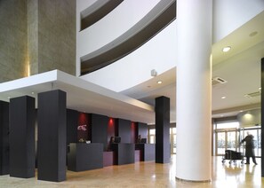 Eine moderne Hotelhalle mit einer Rezeption, einer großen Säule und einem Gepäckwagen.