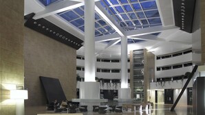 Un hall espacioso con techo alto, tragaluces y una escalera central.