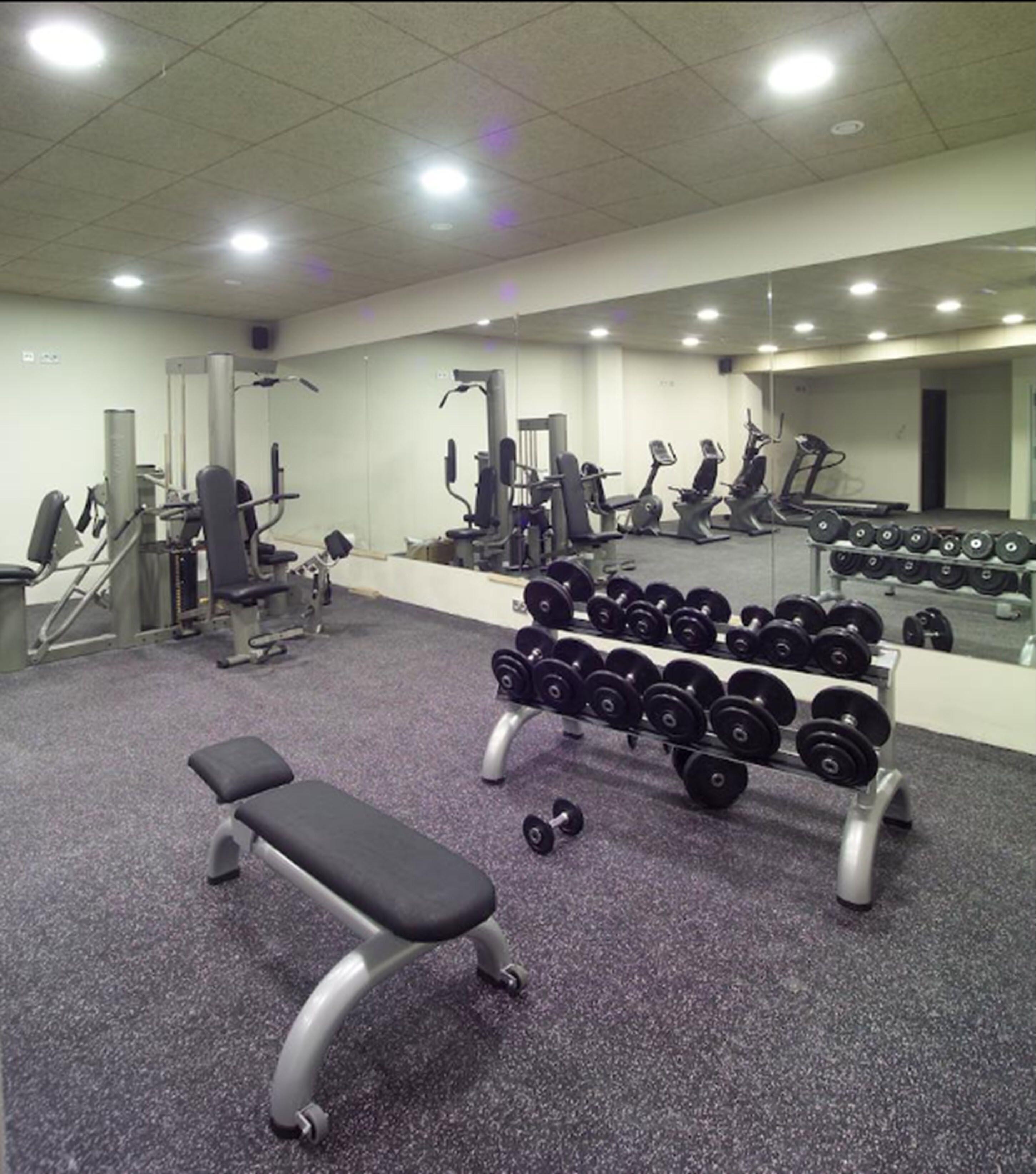 Une salle de sport équipée de divers appareils d’exercice, notamment des haltères, des tapis de course et des appareils de musculation.