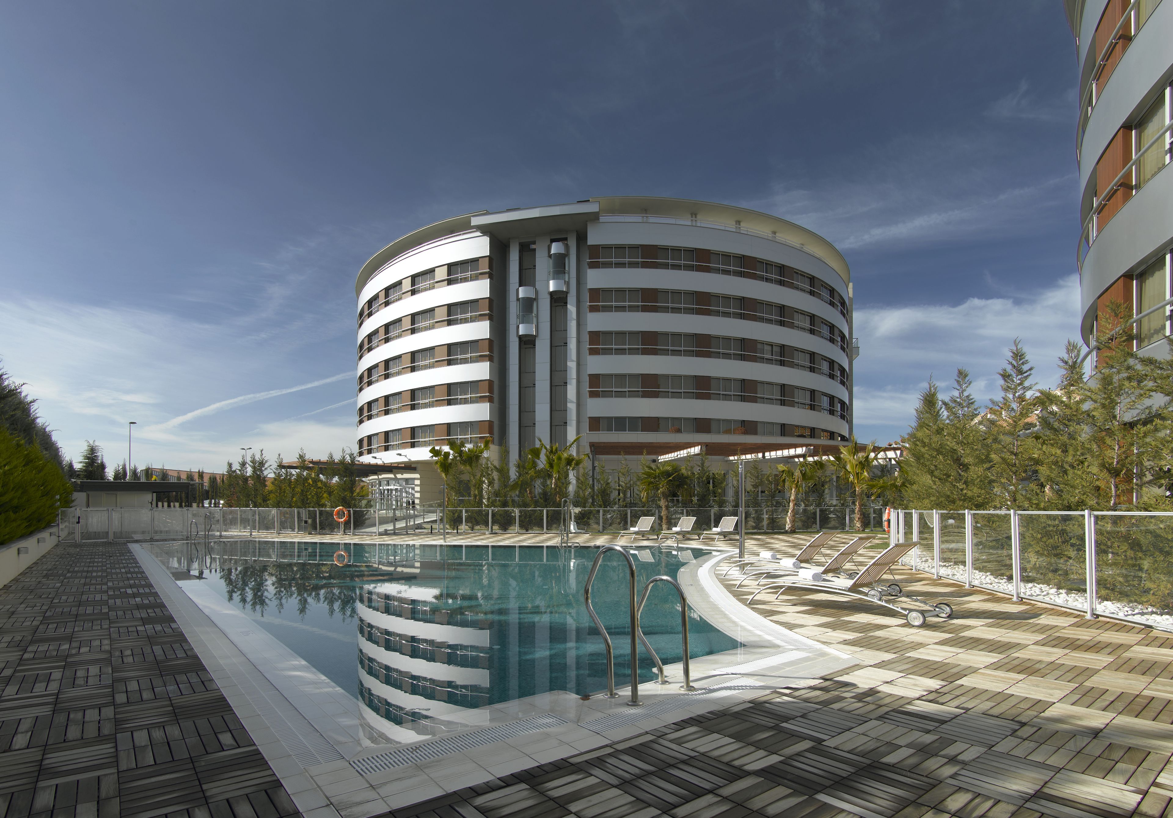 A modern hotel with a circular pool area, lounge chairs, and a clear sky.