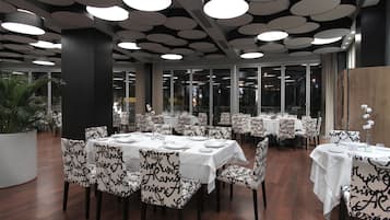 A restaurant with round tables and chairs, large windows, and a modern ceiling design.