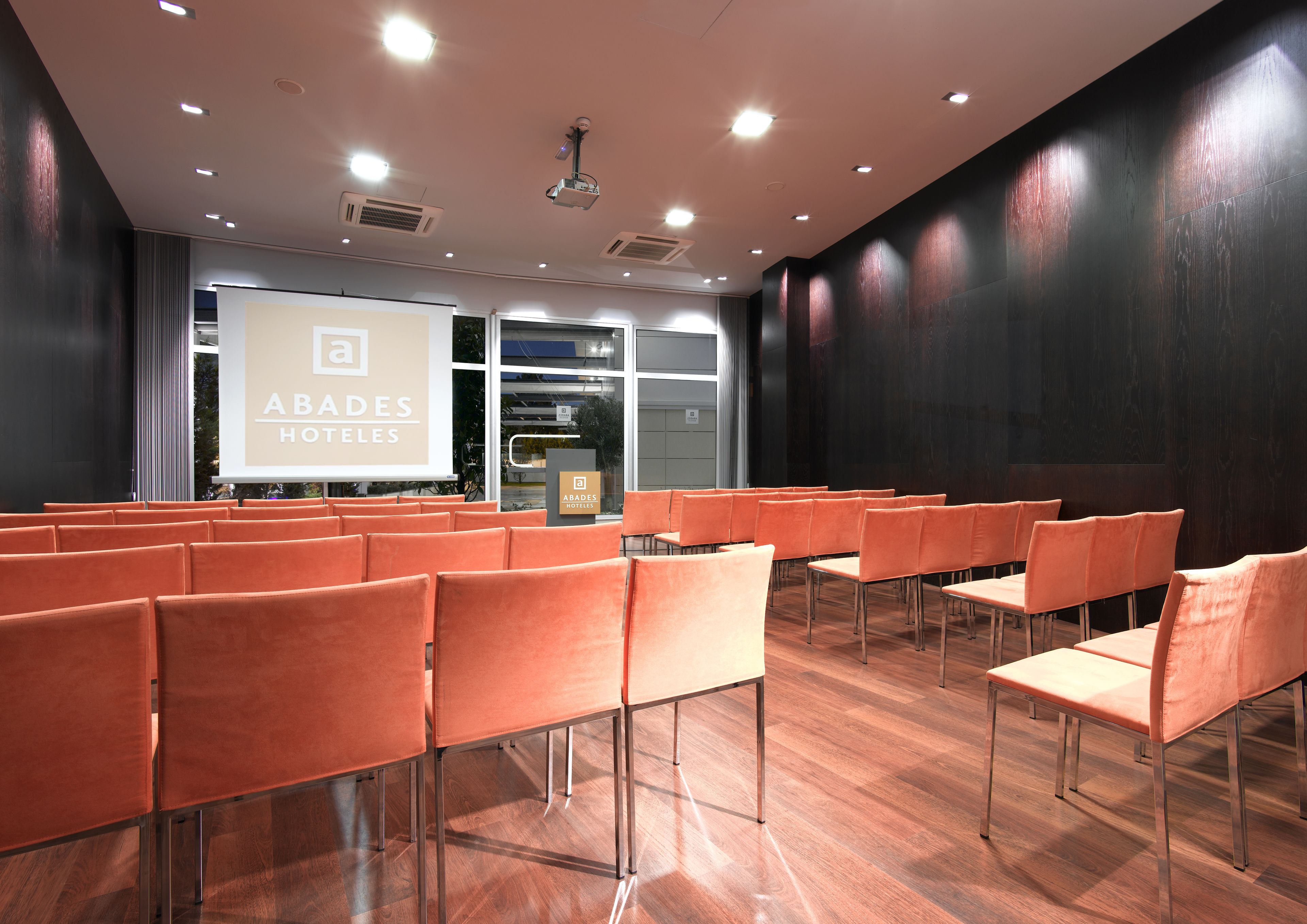 A conference room with rows of orange chairs, a projector screen, and a podium.