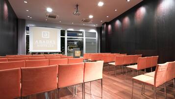 A conference room with rows of orange chairs, a projector screen, and a podium.