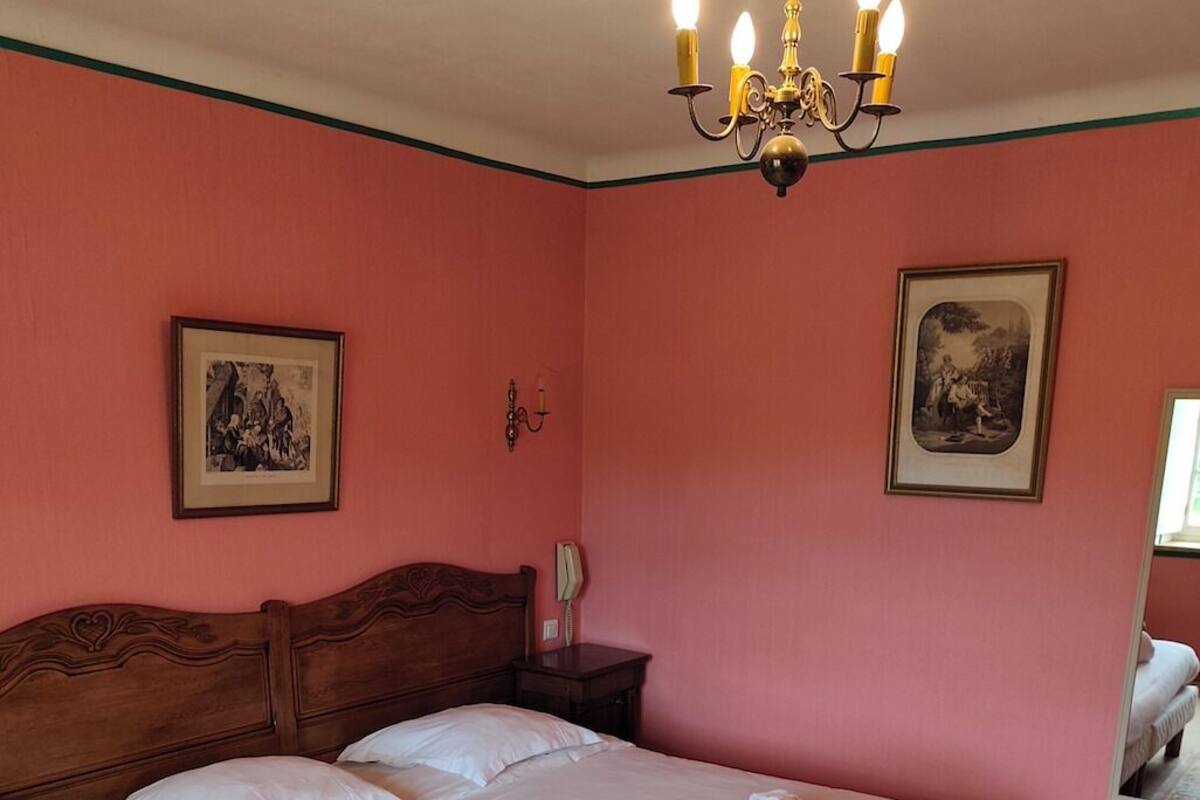 A bedroom with a large bed, a wooden headboard, a chandelier, and two framed pictures on the walls.