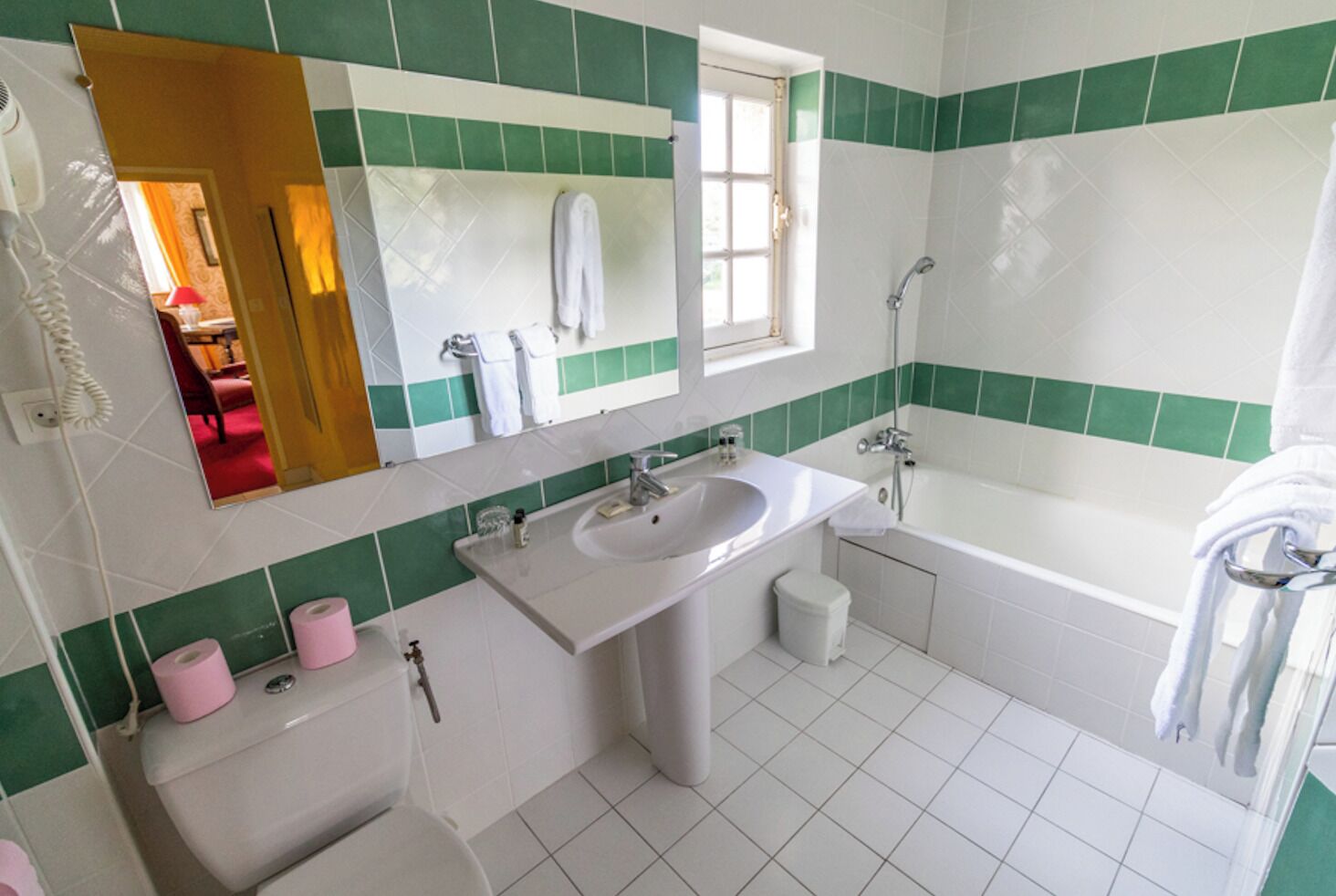 Un baño con lavamanos blanco, una bañera y un inodoro. Las paredes están cubiertas de azulejos blancos y verdes.