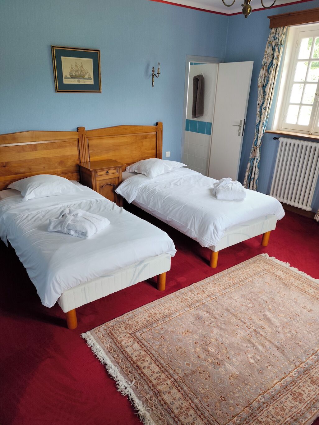 Ein Zimmer mit zwei Einzelbetten, einem Holzkopfende, einem weißen Heizkörper, einer Tür und einem gemusterten Teppich.