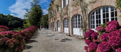A building with arched windows and a gravel pathway lined with pink flowers.