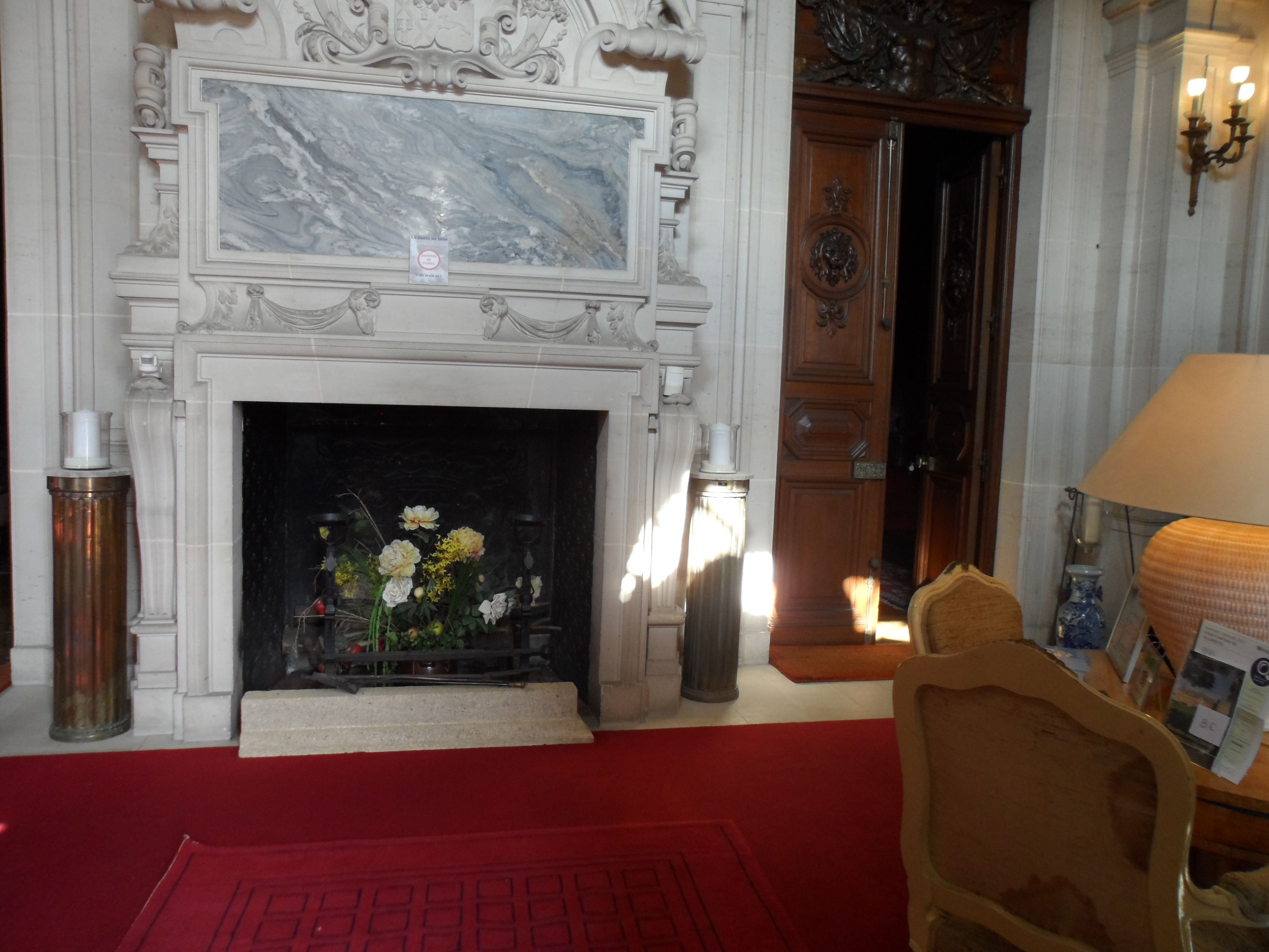 A grand room with a marble fireplace, a red carpet, and a wooden door.