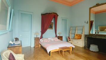 A bedroom with a wooden floor, a bed with a canopy, a chair, a dresser, and a mirror.