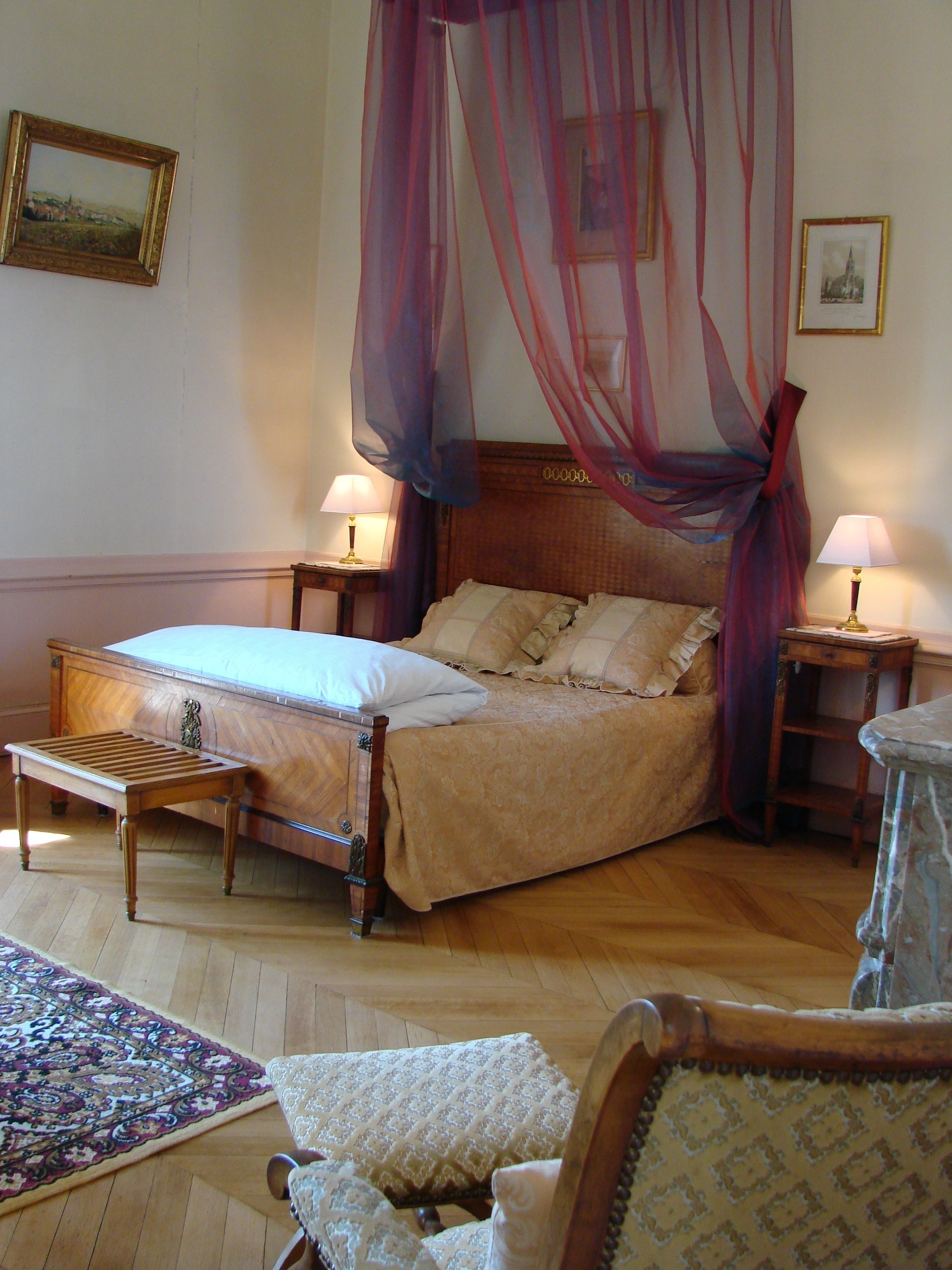 A bedroom with a wooden bed, two bedside tables, a nightstand, a chair, and a patterned rug.