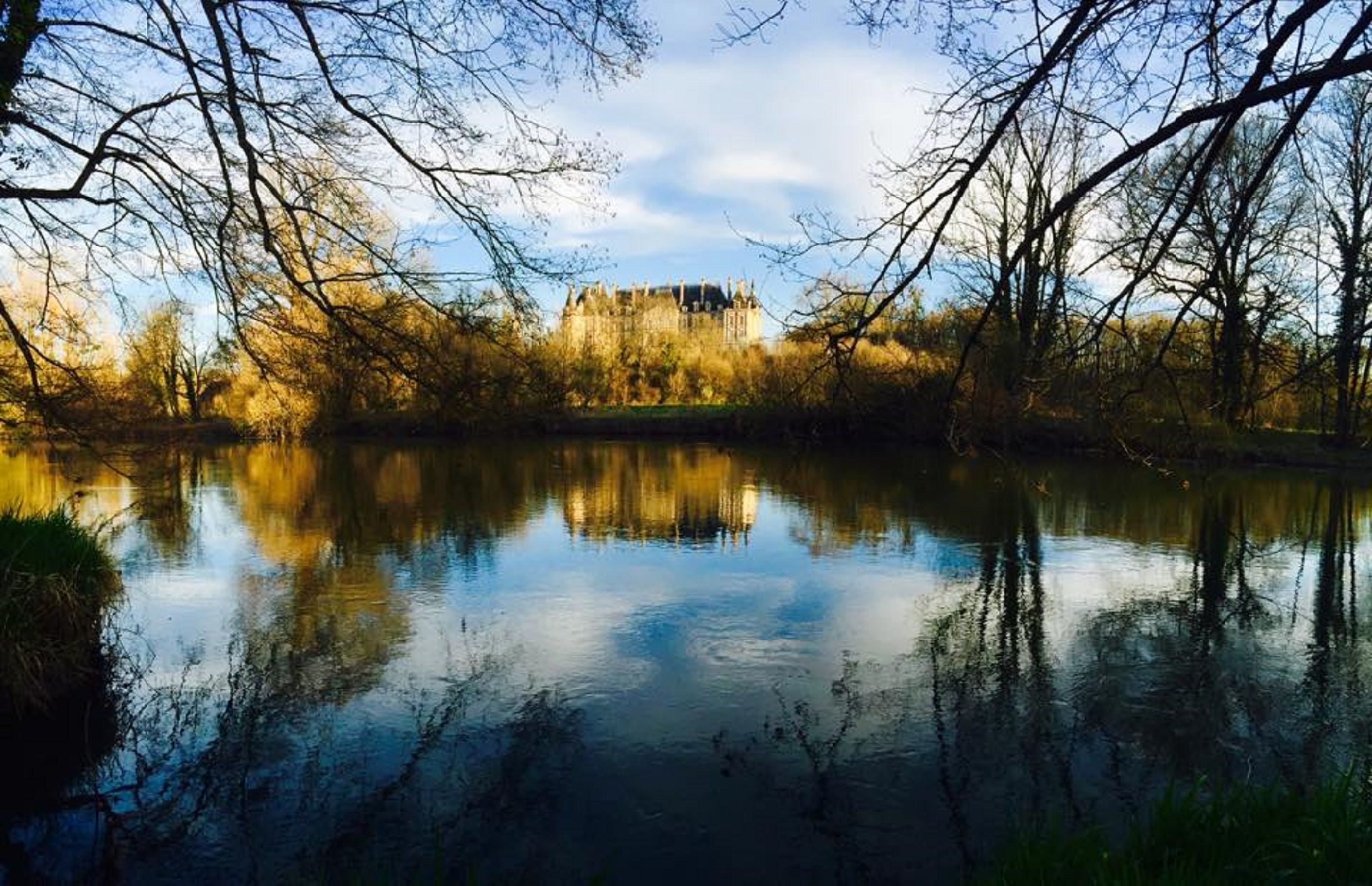 Un castillo reflejado en un río tranquilo, rodeado de árboles.