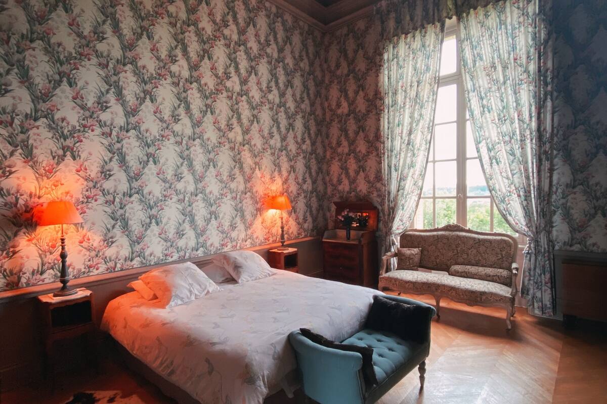 Quarto com cama grande, duas mesas de cabeceira com luminárias, um sofá e janela com cortinas.