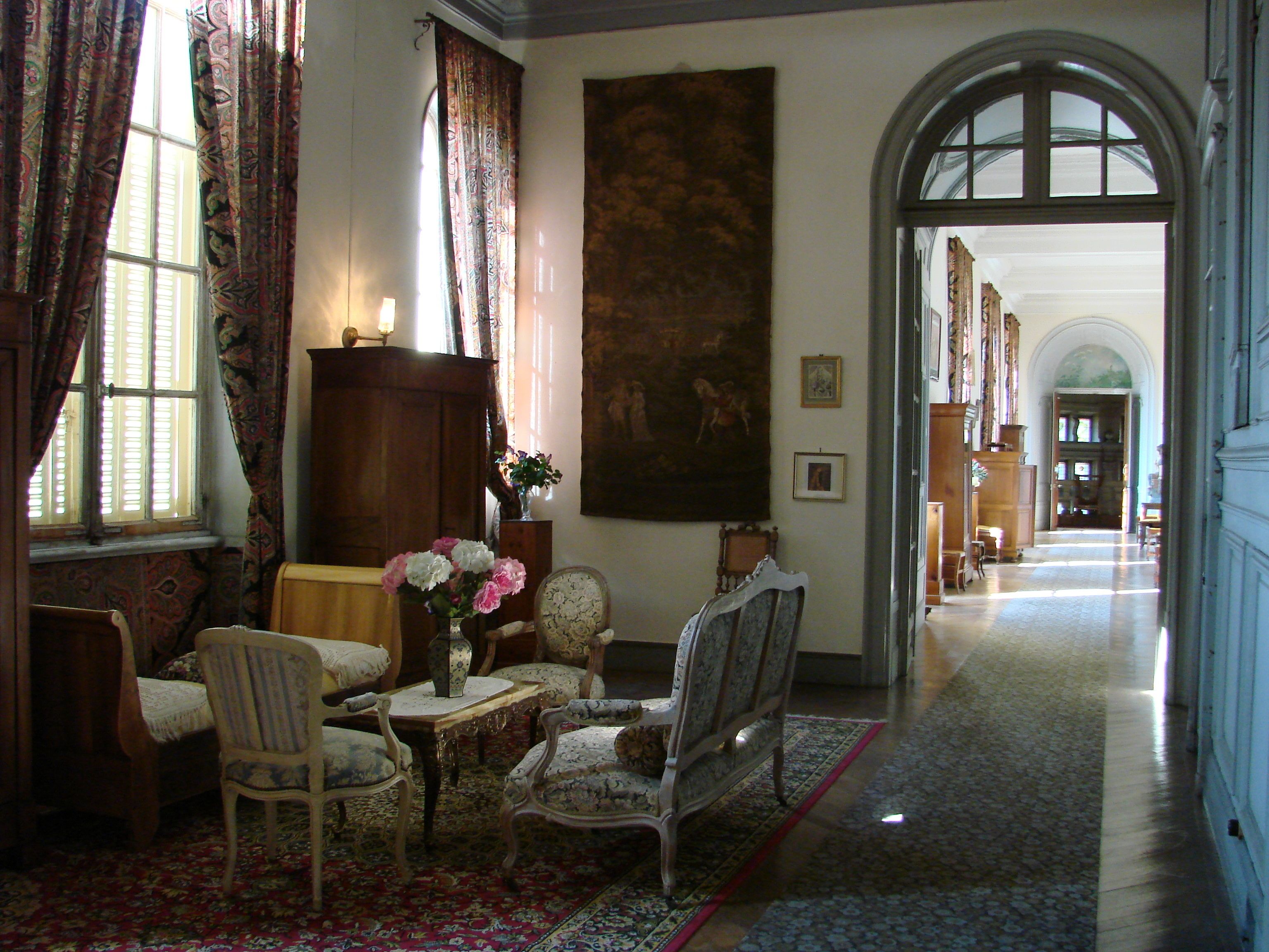A room with a large window, a wooden cabinet, a painting, and a chair.