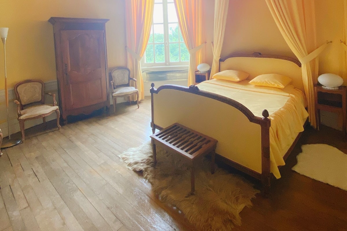 Quarto com cama de madeira, mesa de cabeceira, cadeira, guarda-roupa e janela com cortinas.