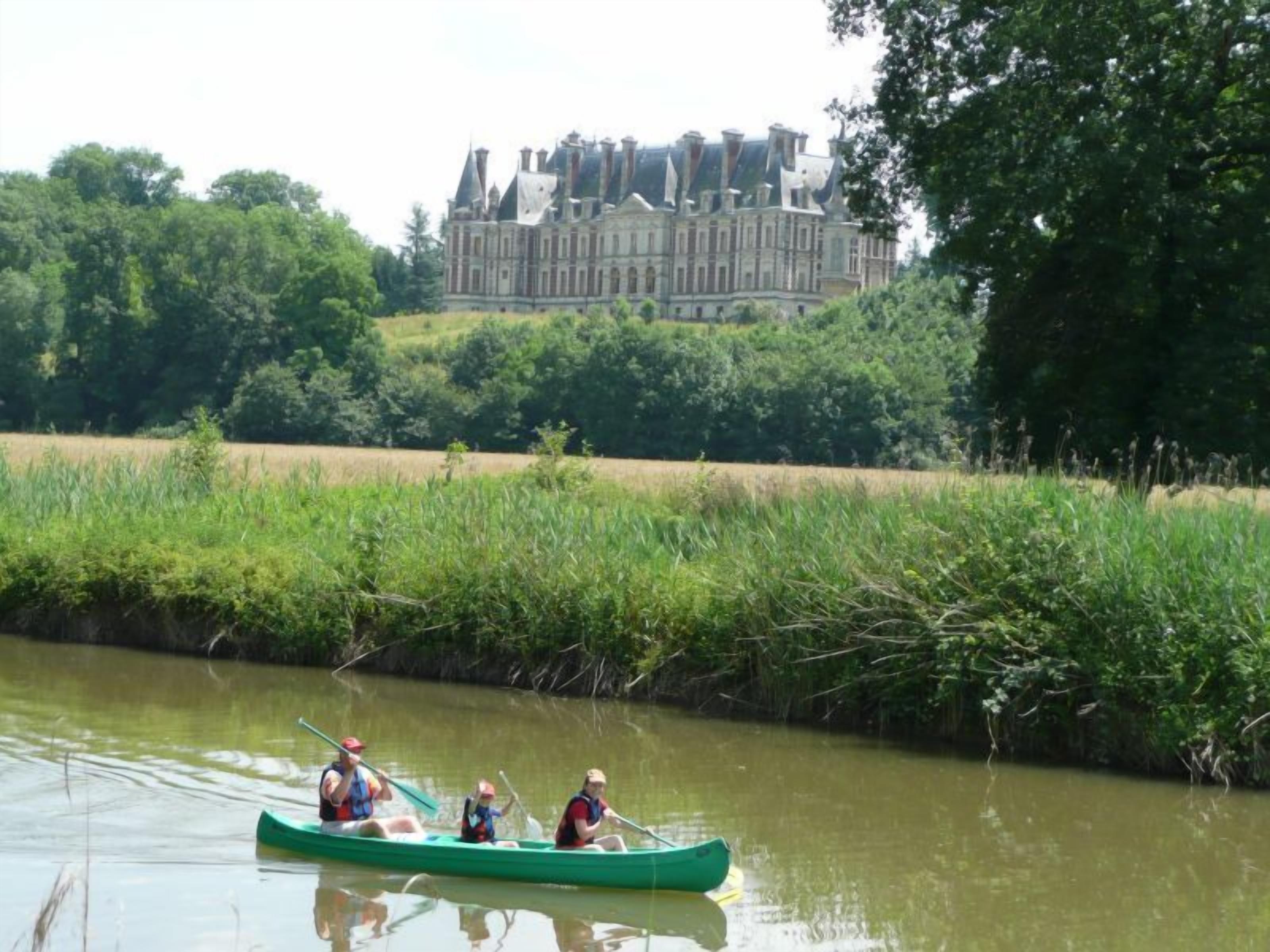 A green canoe on a river with a large building in the background.