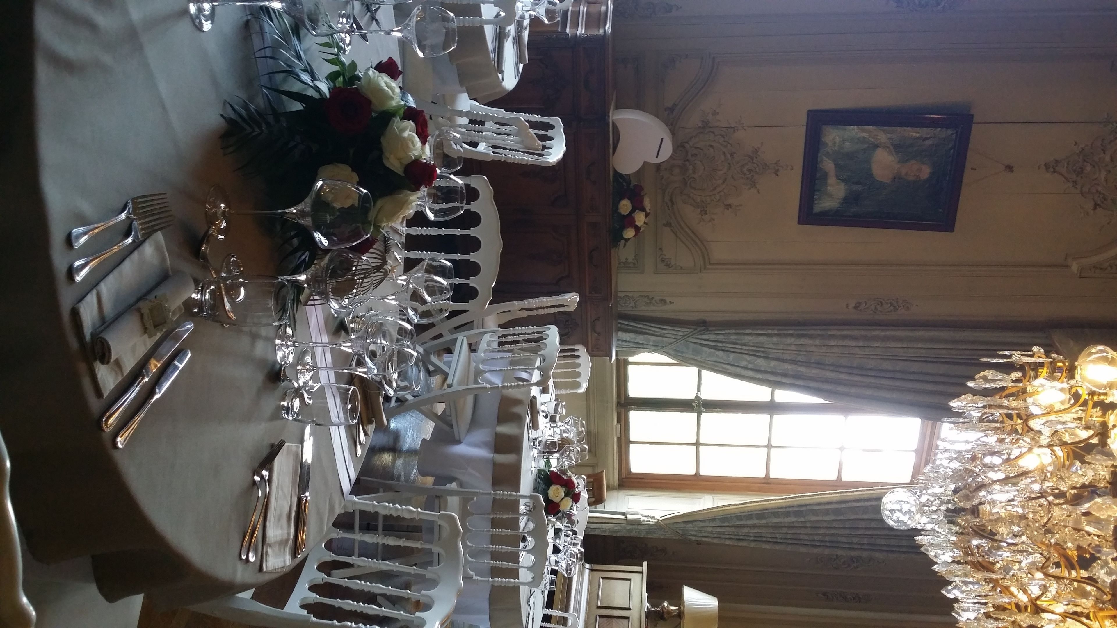 Una mesa de comedor dispuesta con varias copas de vino, tenedores, cuchillos y un centro de mesa con rosas rojas y blancas.