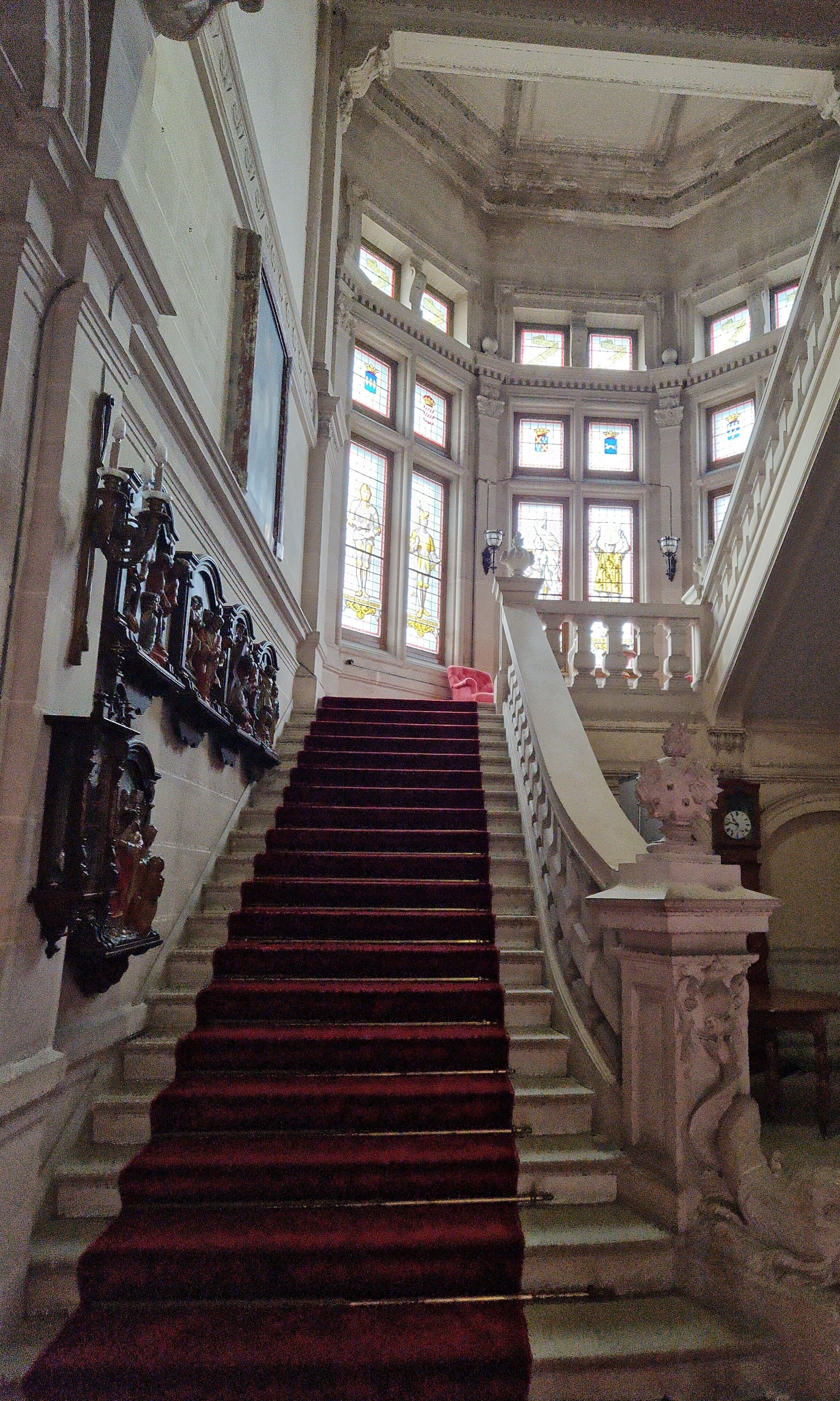 A grand staircase with a red carpet, ornate wall decorations, and large stained glass windows.