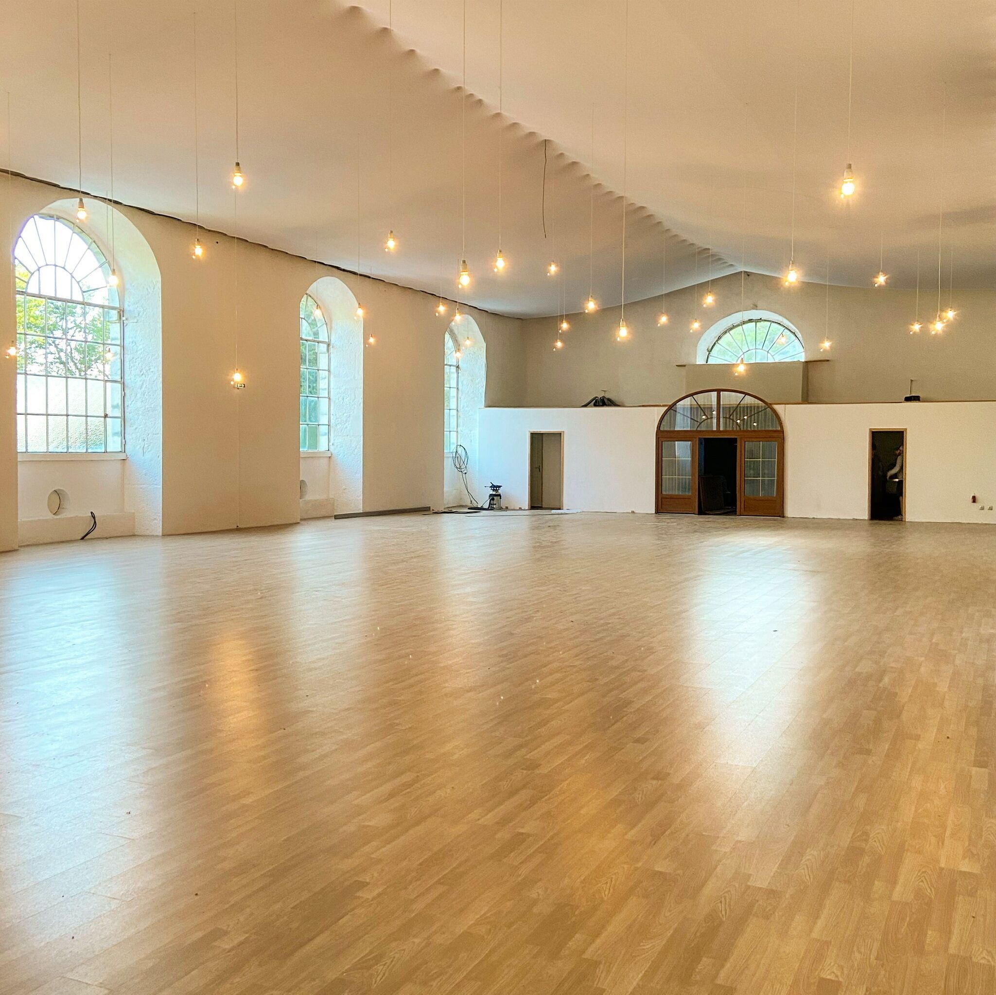 A spacious hall with high ceilings, large arched windows, and hanging light fixtures.