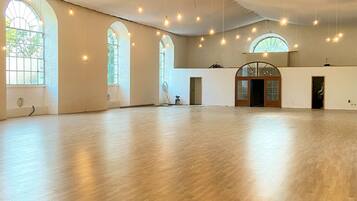 A spacious hall with high ceilings, large arched windows, and hanging light fixtures.