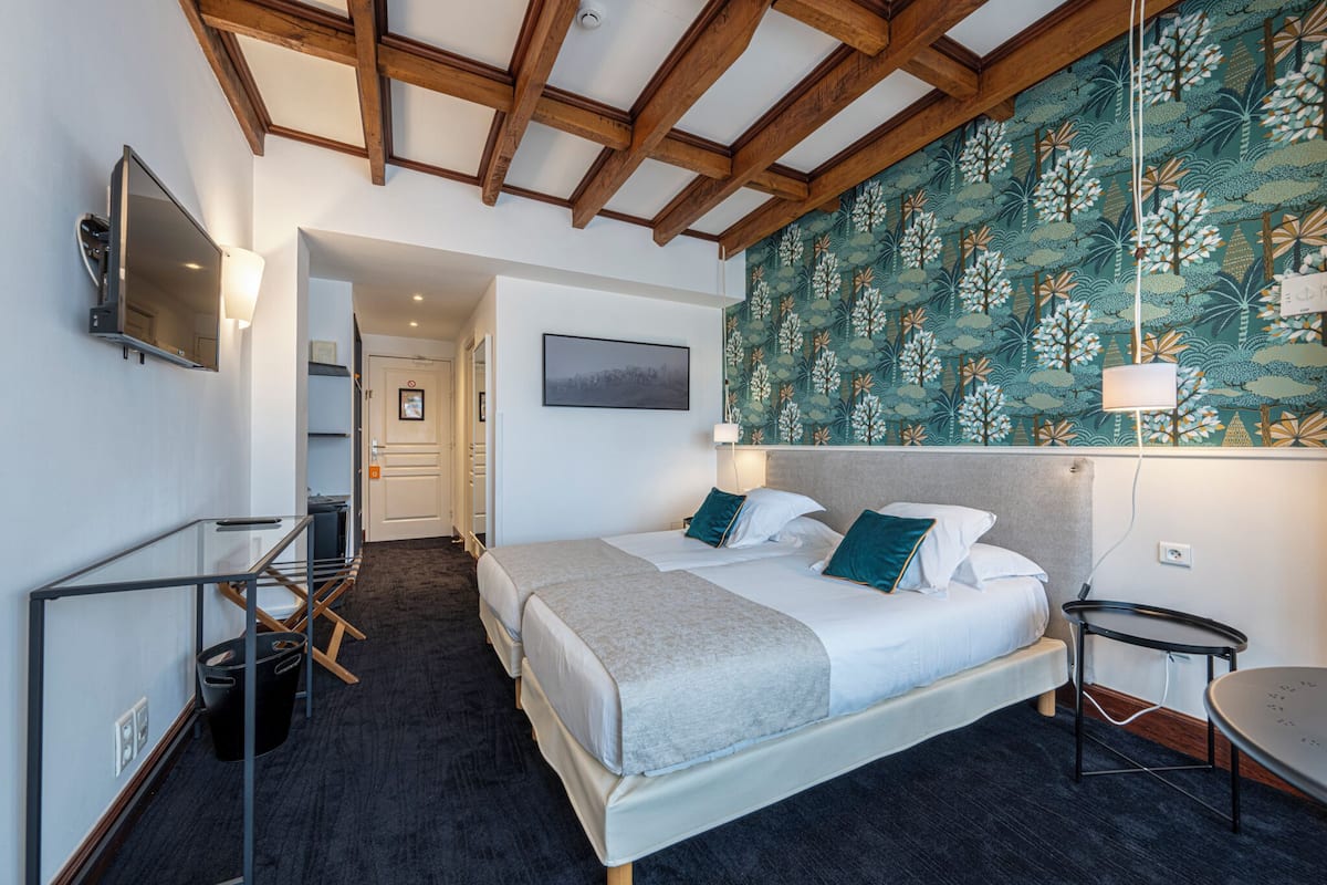 A hotel room with a large bed, a desk, a chair, a TV, and a wall with a floral pattern.