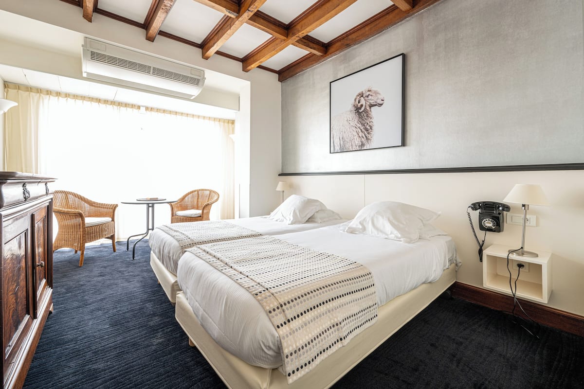A hotel room with two beds, a desk, a chair, a small table, and a wall-mounted telephone.