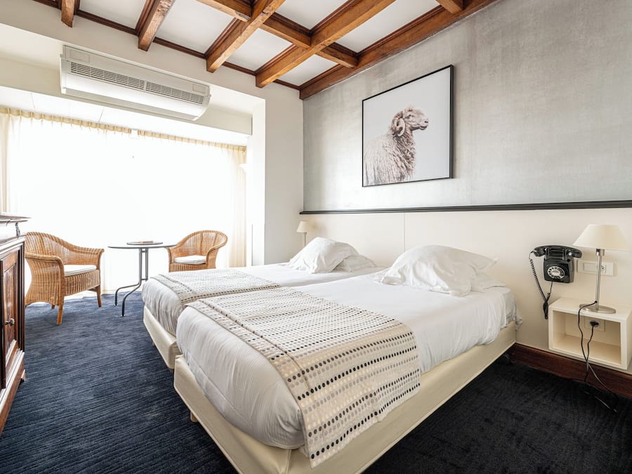 Een hotelkamer met twee bedden, een bureau, een stoel, een klein tafeltje en een telefoon aan de muur.