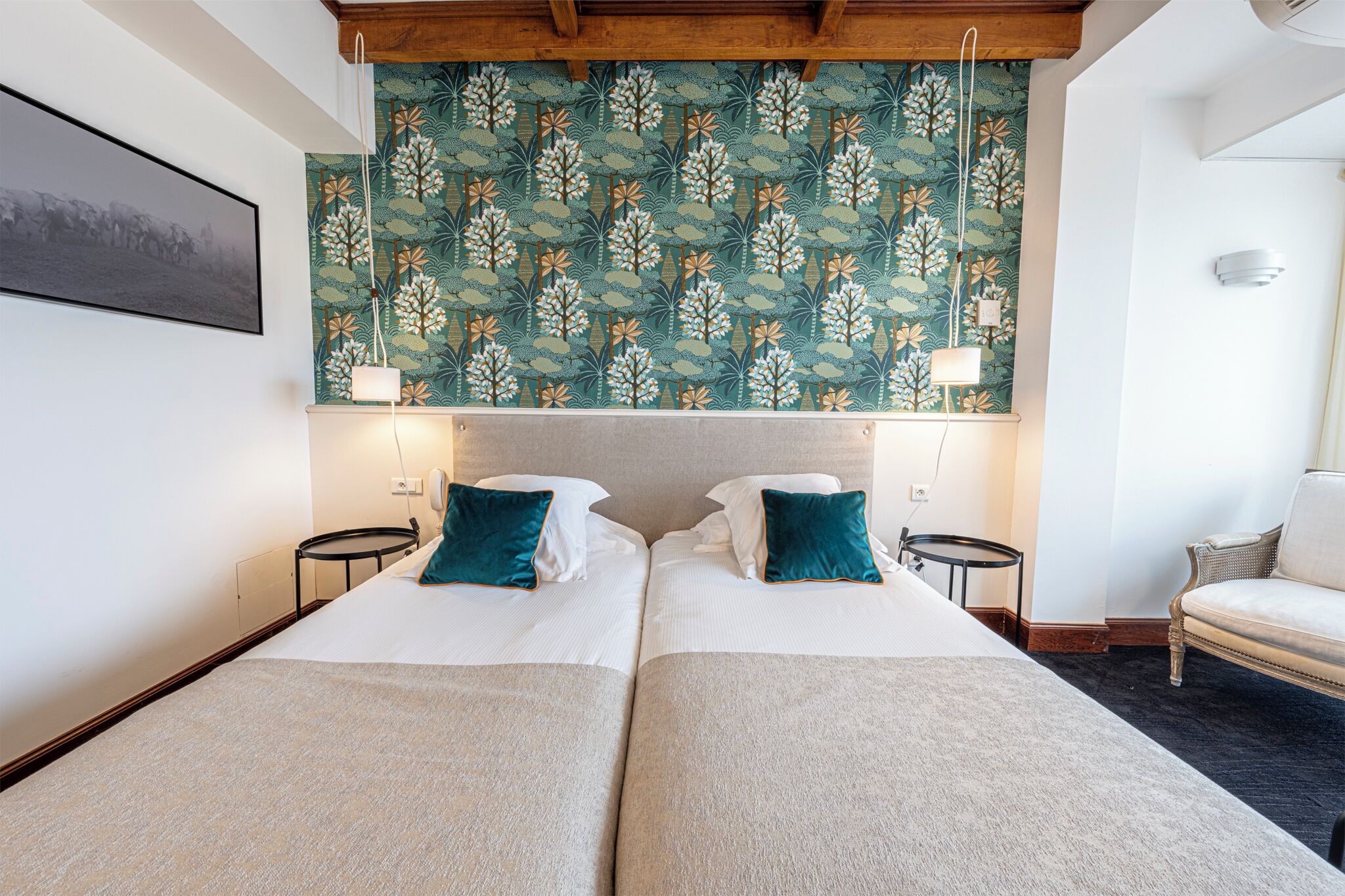Quarto de hotel com duas camas, papel de parede estampado, um quadro na parede e uma cadeira.