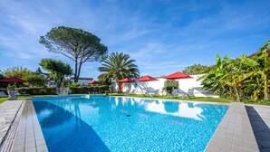 A swimming pool with red umbrellas, lounge chairs, and palm trees. - Hôtel Ithurria (Ainhoa)