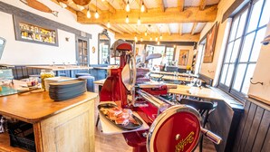 A restaurant interior with wooden tables, a red meat slicer, and a bar area. - Hôtel Ithurria (Ainhoa)