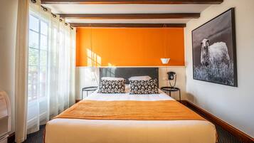 Habitación de hotel con una cama grande, dos mesitas de noche, una ventana con cortinas, una pared de acento color naranja y un cuadro en la pared.