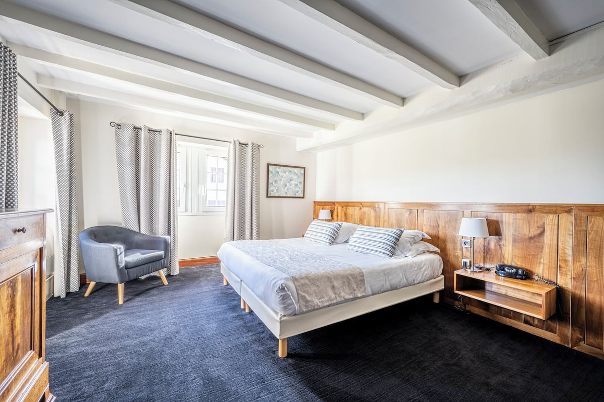 A bedroom with a bed, a chair, a nightstand, and a wooden headboard.