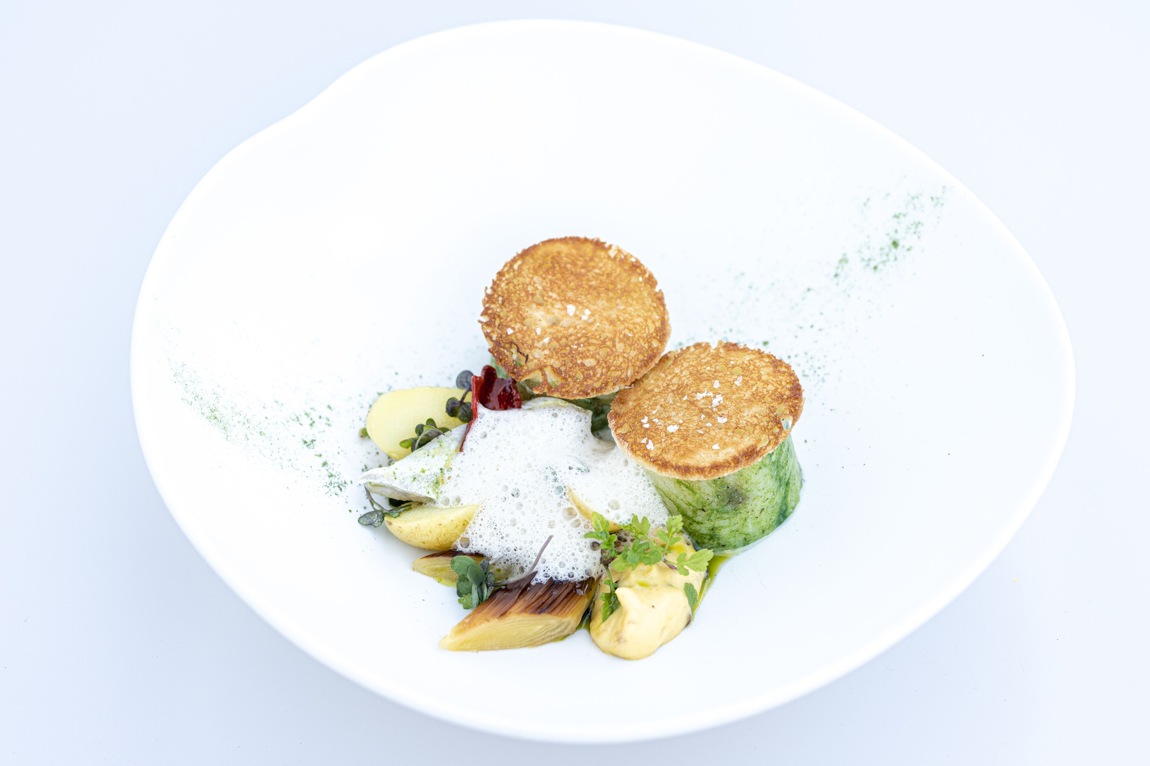 A white plate with a salad, two round items, and a dollop of cream.
