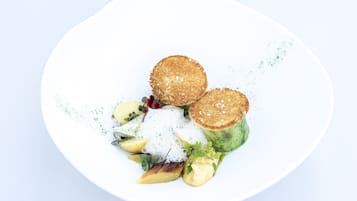 A white plate with a salad, two round items, and a dollop of cream.