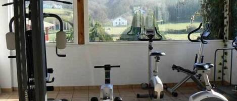 A gym with exercise equipment and a large window with a view of a house and mountains.