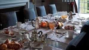 A dining room with a table set for breakfast, including plates, cups, and a variety of food items.
