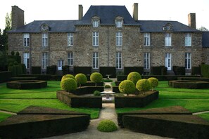 A large stone building with symmetrical windows and a central garden with neatly trimmed hedges.