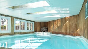 An indoor swimming pool with wooden walls and a stone sculpture. - Villa Louise (Aloxe-Corton)