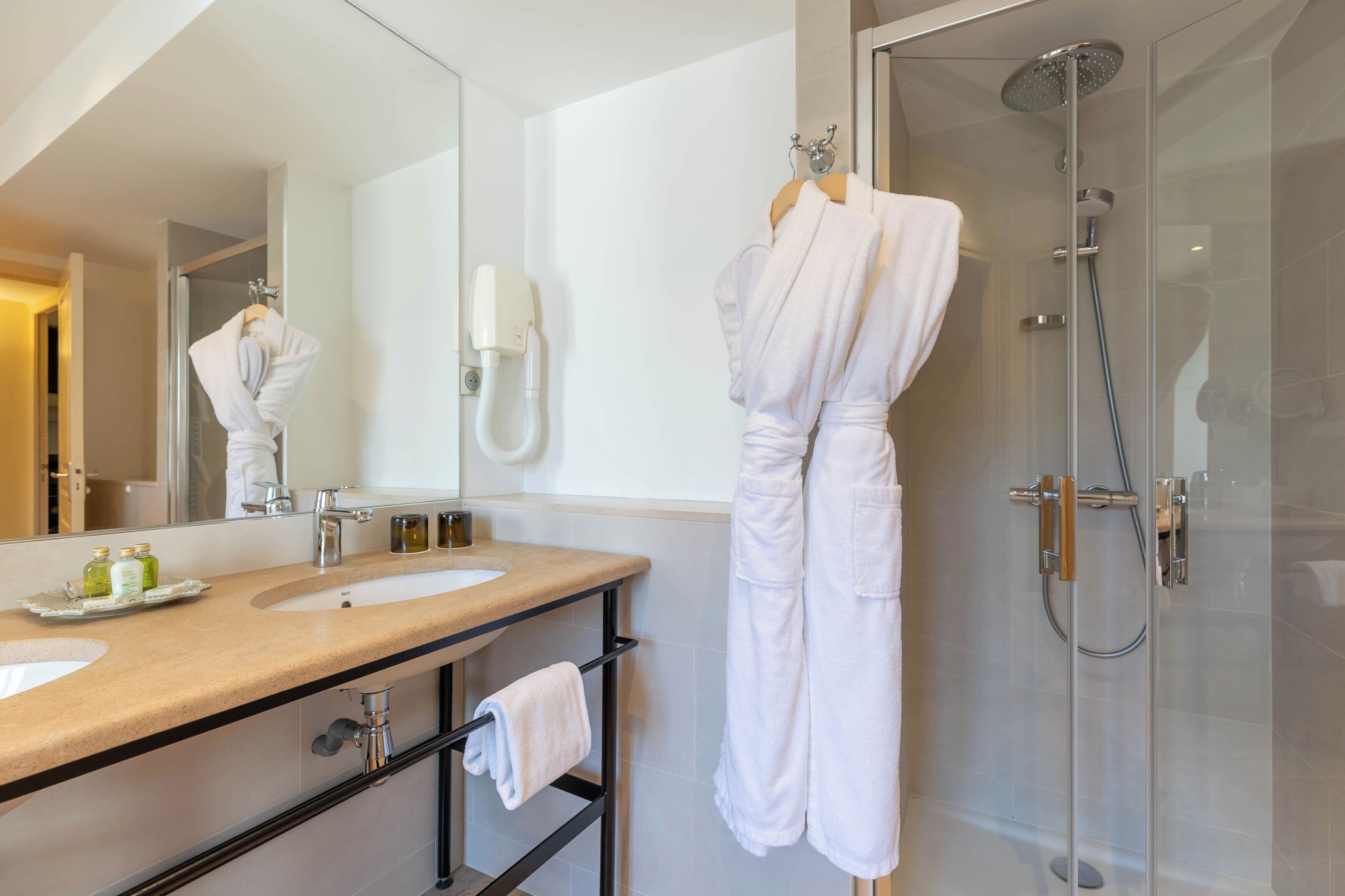A bathroom with a double sink, a mirror, a glass shower enclosure, and a robe hanging on a rack.