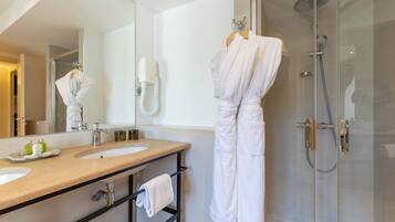 A bathroom with a double sink, a mirror, a glass shower enclosure, and a robe hanging on a rack.