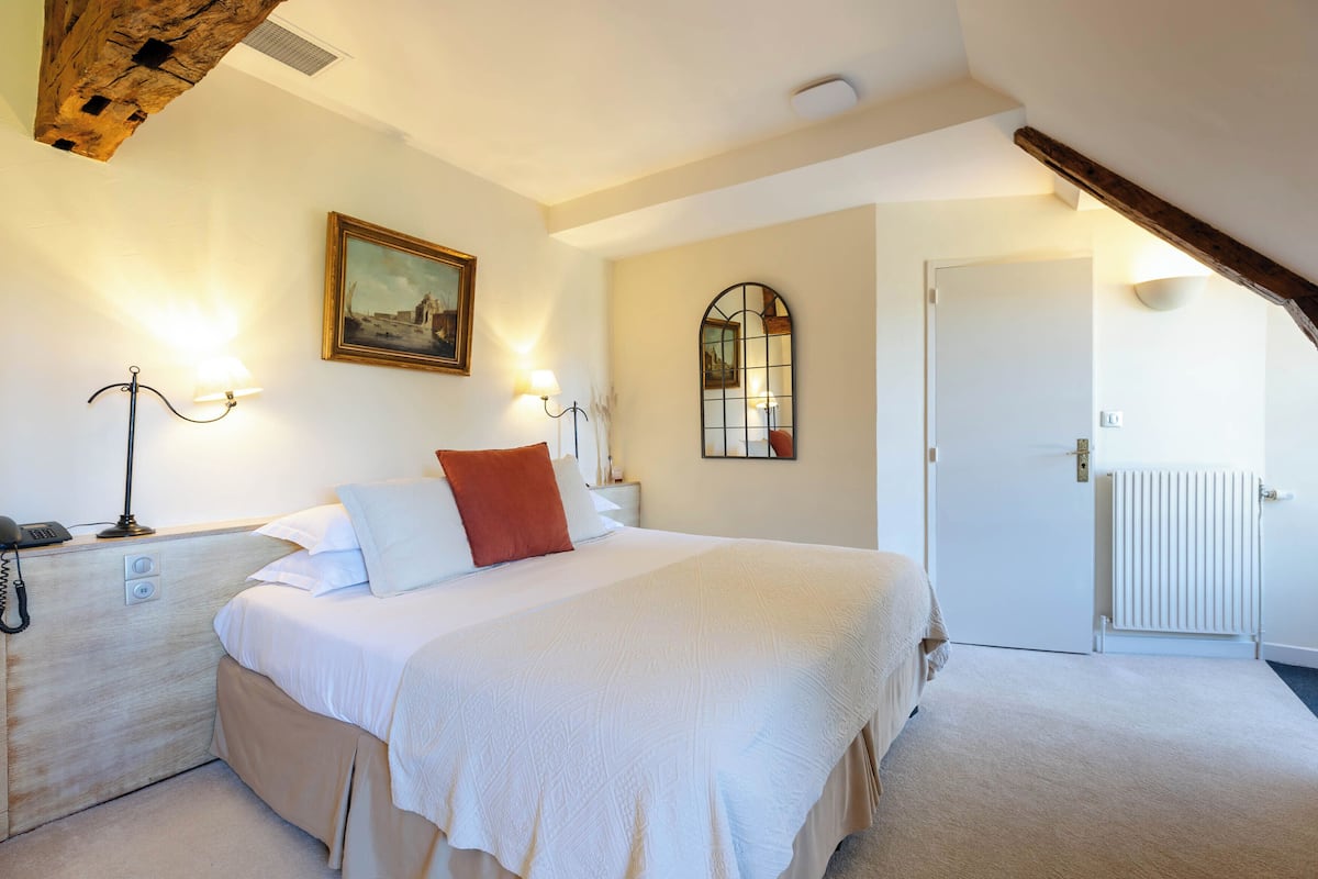 A bedroom with a bed, bedside lamps, a painting, a mirror, and a radiator.