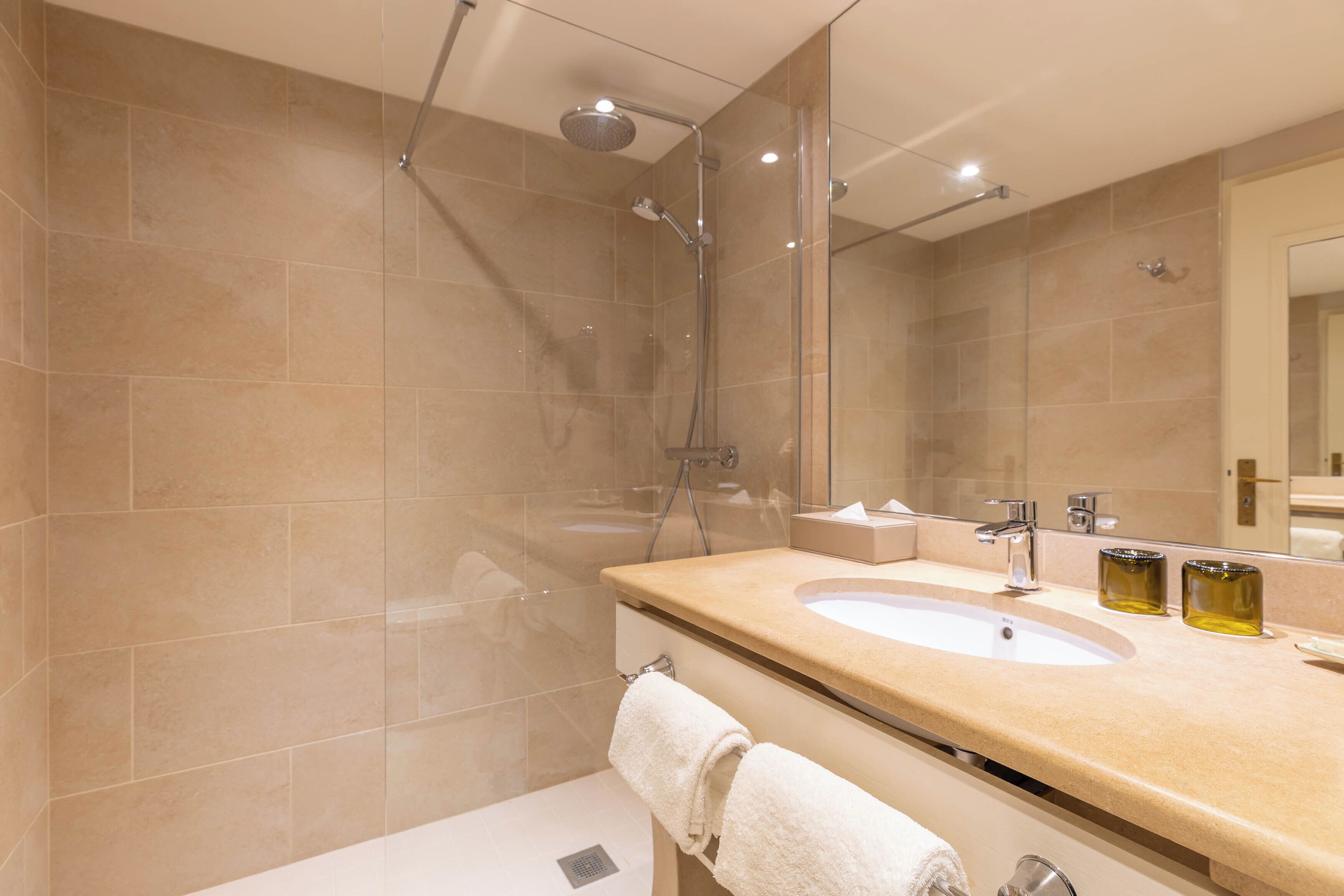 Un baño moderno con ducha envuelta en vidrio, lavabo con espejo y toallero.