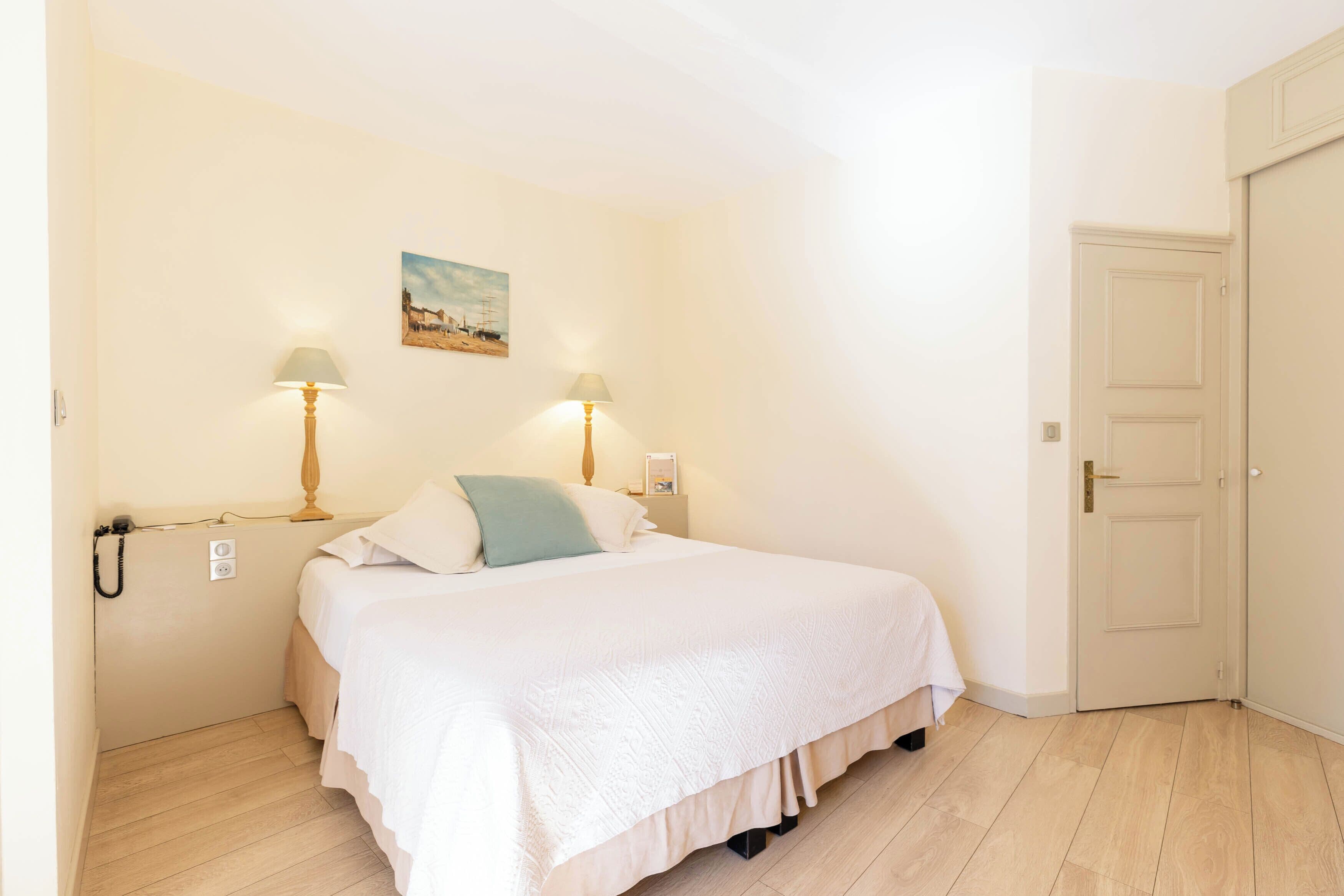 Una camera da letto con un letto, due lampade sui comodini, un quadro appeso e una porta.
